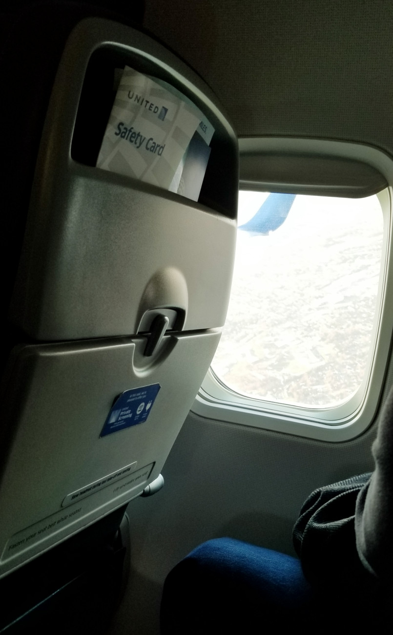 A photo taken inside a plane looking out from the window at a sprawling city overhead.