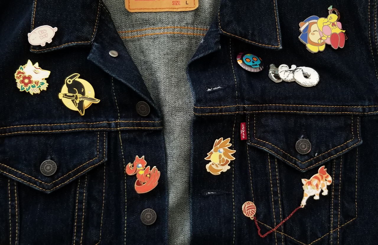 Close up of top half of a denim jacket. Showing off various pins.