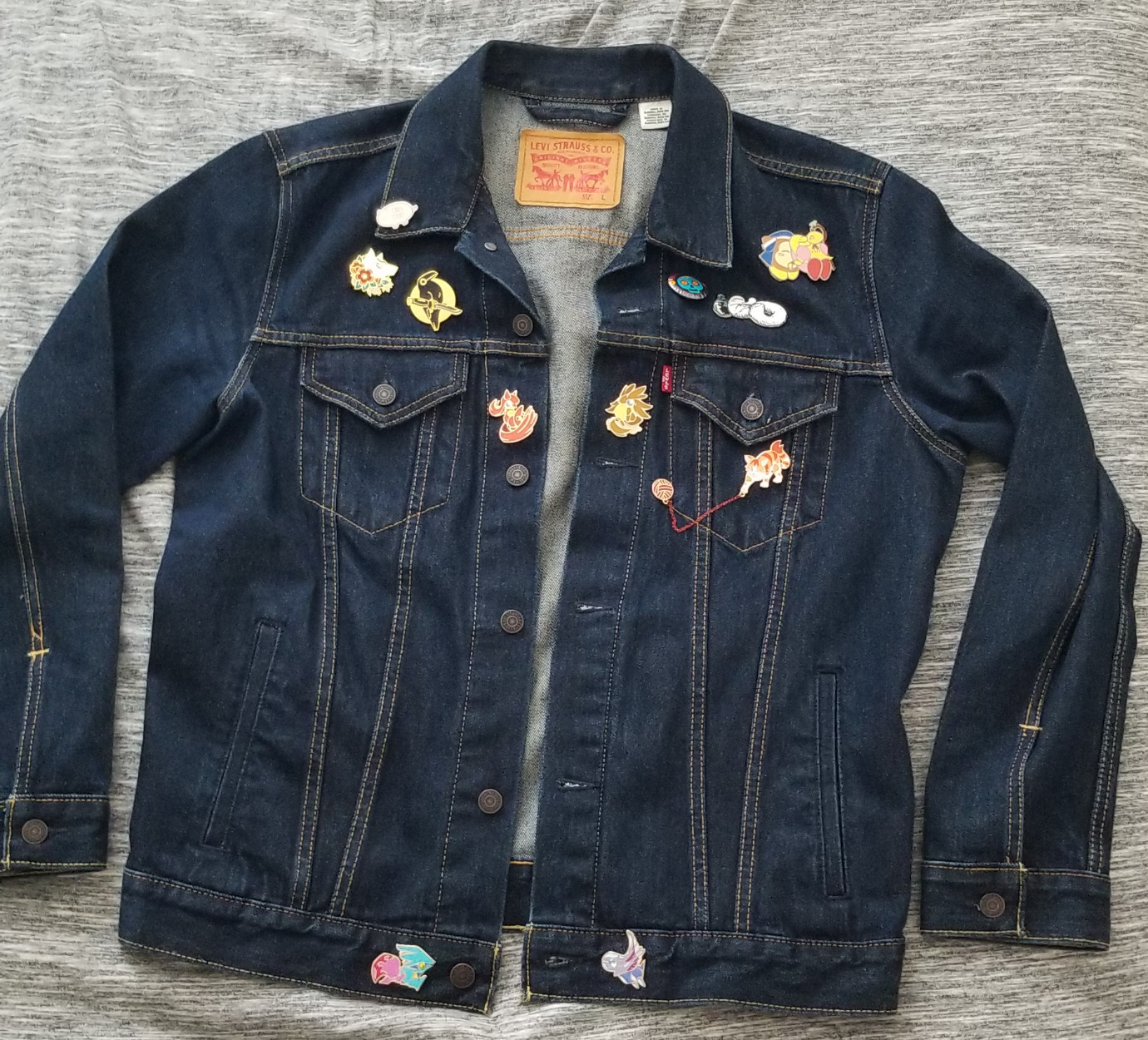 A denim jacket adorned with various enamel pins.