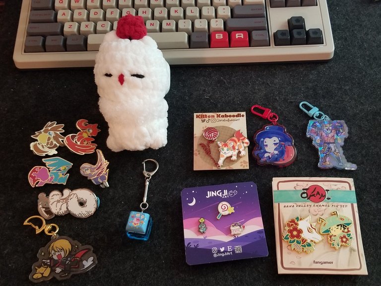 Various enamel pins, acrylic charms, keychain, and a crochet plushie.
